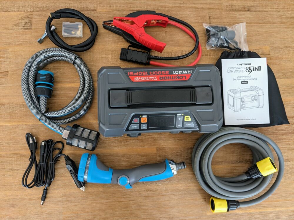 Top-down view of the Lokithor AW401 portable jump starter with all of its accessories arranged around it, including  two water hoses, an air hose, jumper cables, a drawstring bag and instruction manual, an adjustable nozzle for the water hose, and bags of connectors and adapters.