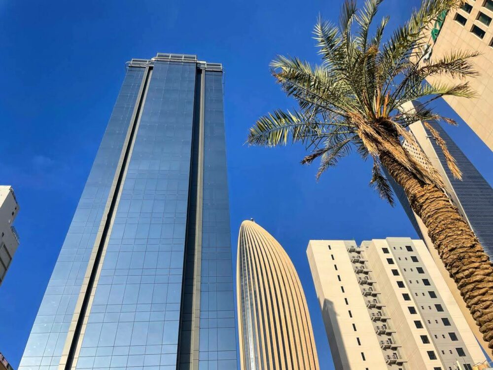 Looking up at tall modern buildings, near a palm tree in Kuwait City