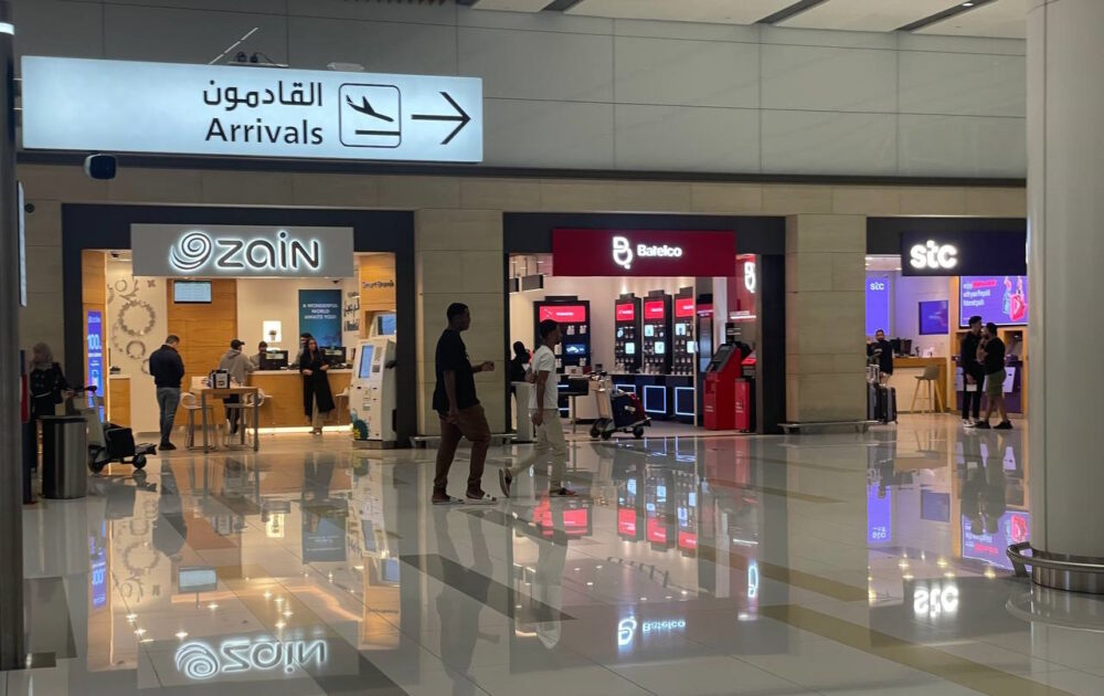 Phone stores from Zain, Batelco, and STC at Bahrain airport, with people walking in front of them