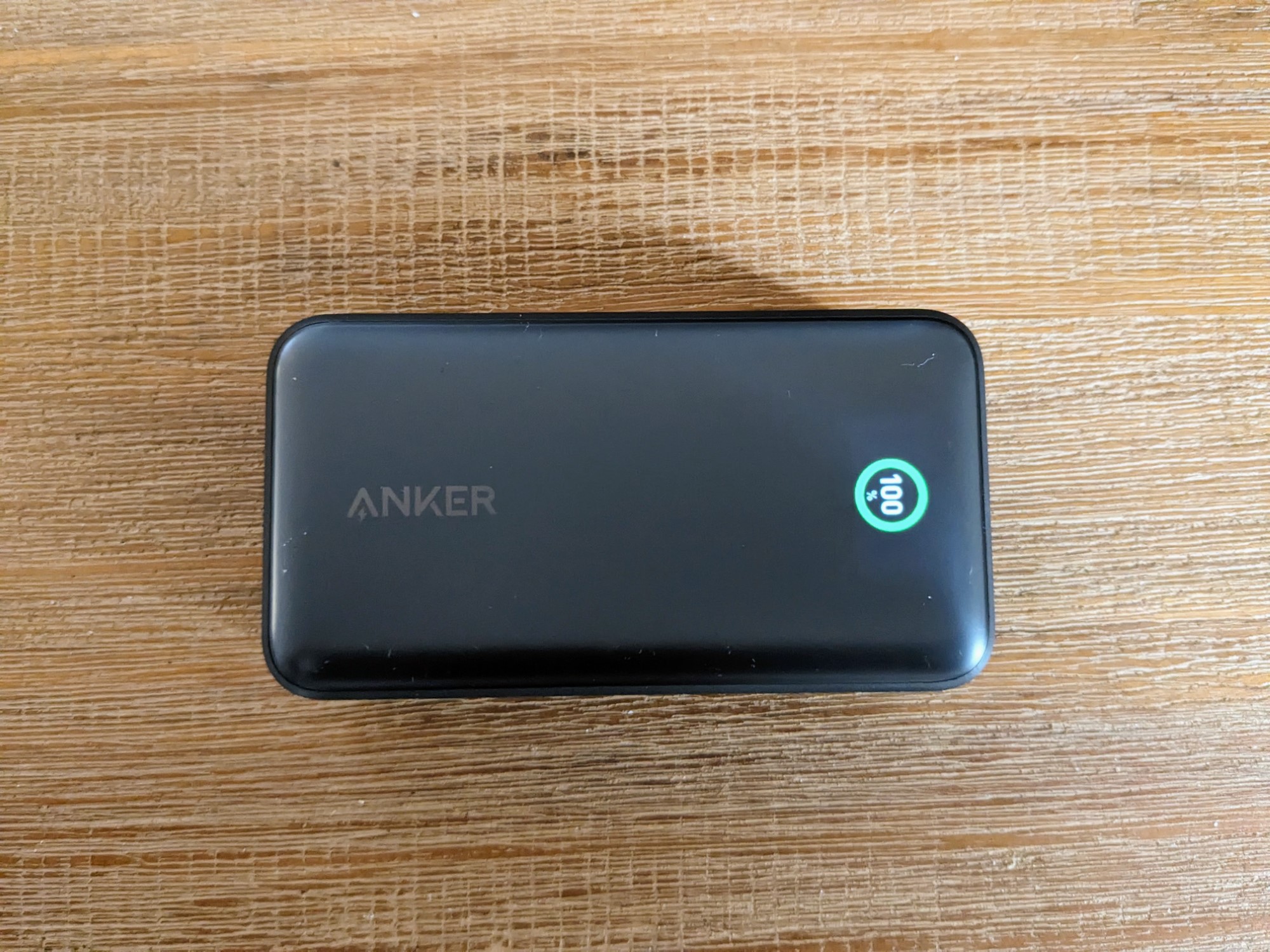 Power bank on wooden table with Anker branding and showing 100% charge
