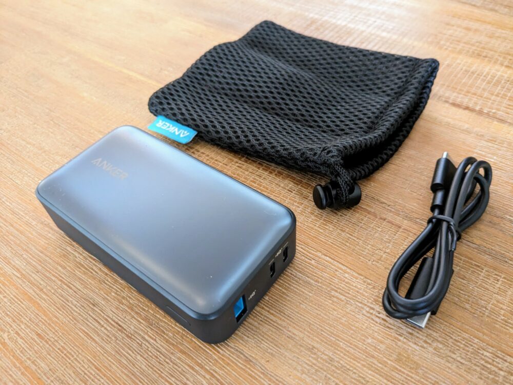 Anker power bank on wooden table with a soft travel pouch and USB cable alongside