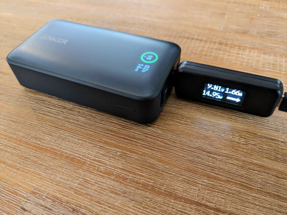 Anker 533 power bank on wooden table with power tester attached showing 14.95W