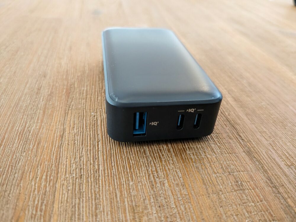 End-on view of a power bank on a wooden table, with two USB C ports and one USB-A port