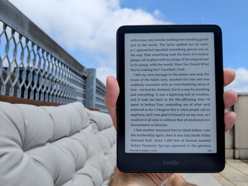 Kindle Paperwhite being held in hand by a person lying on an outdoor sofa