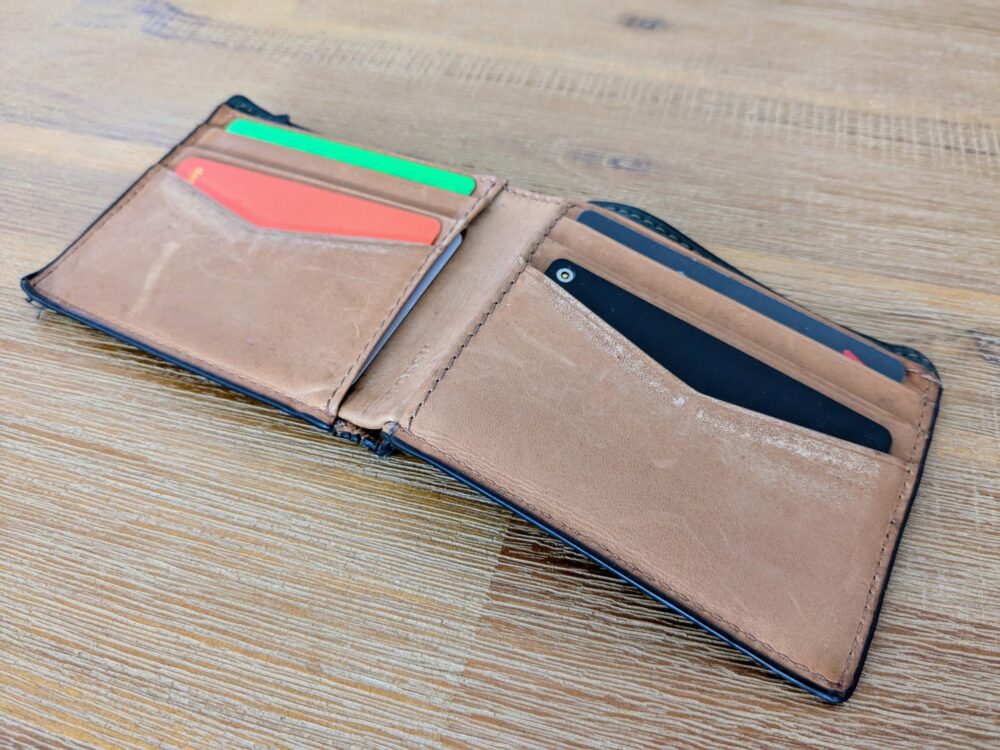 Open brown leather wallet on wooden table with credit cards and a black tracker visible